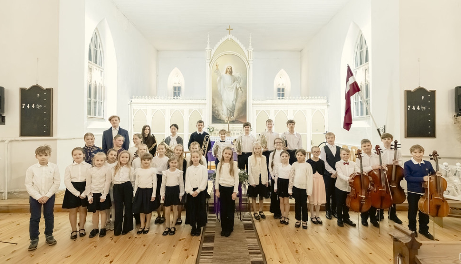 Audzēkņi pēc koncerta altāra priekšā nostājušies ar instrumentiem rokās